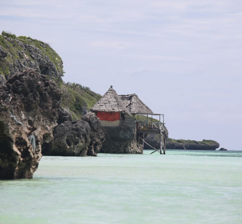 Thatched hut on rocky cliffs at Mtende Beach Zanzibar with clear shallow ocean water and rugged coastline